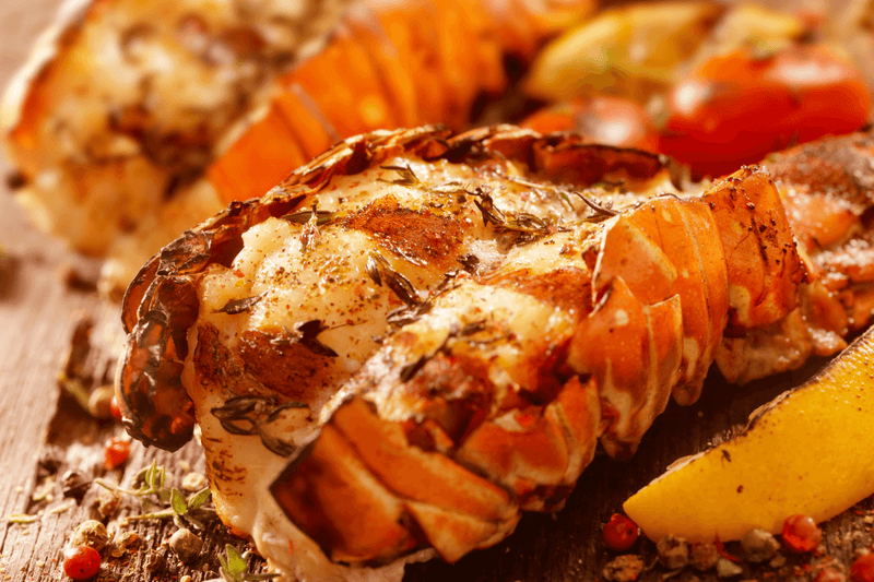 Grilled lobster tails on BBQ grates with golden char and butter glaze.