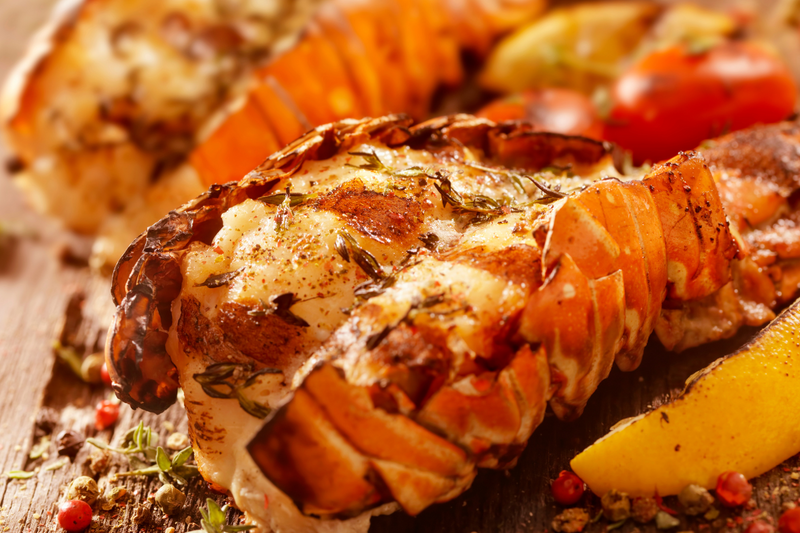 Grilled lobster tails on BBQ grates with golden char and butter glaze.