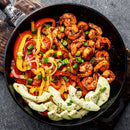 A skillet filled with cooked shrimp, sautéed red and yellow bell peppers, onions, and sliced cucumbers, all topped with chopped green onions for a vibrant Caribbean-inspired dish. Finish it off with The Spice Lab Scotch Bonnet Sea Salt for the perfect touch of flavorful heat.