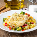 A white plate features a seasoned fish fillet atop mixed vegetables—broccoli, green beans, red peppers, and potatoes. Bottles of oil and a salt shaker sit in the background on a wooden table. The dish is enhanced with The Spice Lab Lemon Juice Powder from The Spice Lab brand, providing a consistent lemon flavor throughout every bite.