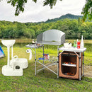 Outdoor camping setup featuring the DirectDeals Foldable Outdoor BBQ Portable Grilling Table With Windscreen Bag, plus portable sink and storage cabinet near a tent by a lake with trees and mountains in the background.