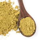 A wooden spoon filled with light brownish-green powder rests on a white surface beside a small pile of the same powder—perfectly capturing the earthy tones of The Spice Lab Ground Oregano, a classic Mediterranean herb and everyday seasoning from The Spice Lab.