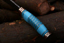 A close-up of the Texan Knives Hand Made Damascus Steel Beautiful Hunting and Camping Knife with smooth blue and gold handle bands, displayed on dark brown logs. Includes an original handmade leather cover. Gift for Him, Christmas Gift.