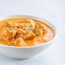 A white bowl filled with creamy orange chicken curry, garnished with The Spice Lab Whole Leaf Cilantro by The Spice Lab, sits on a light gray surface.