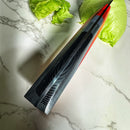The Spaceman Knives EM Wave Chef Knife by Spaceman Knives, featuring a modern textured Damascus steel blade, rests on a marble countertop beside two pieces of iceberg lettuce.