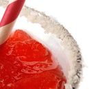 Close-up of a red icy drink in a glass rimmed with The Spice Lab Traditional Margarita Salt Cocktail Rimmer by The Spice Lab, featuring a red and white striped straw and set against a white background.