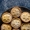 A plate of round mince pies topped with star-shaped pastry and dusted with powdered sugar, with extra sugar sprinkled on a dark background—a perfect centerpiece for your holiday baking, especially when finished with a hint of The Spice Lab Organic Ground Nutmeg to enhance the festive flavor.