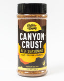 A plastic jar of Chiles and Smoke Canyon Crust Beef Seasoning features salt, pepper, and garlic in an 11.5 oz black, yellow, and brown label with cactus graphics and the text “Premium BBQ Rub.” This bold blend is perfect as a steak seasoning or brisket rub.