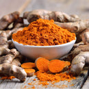 A white bowl brimming with vibrant orange The Spice Lab Golden Milk Turmeric Tea Superfood Premium Powder 4 oz sits atop a wooden surface, surrounded by whole and sliced turmeric roots—an essential ingredient from The Spice Lab for any golden milk turmeric tea or superfood powder blend.