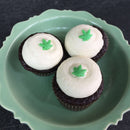 Three chocolate cupcakes with white frosting, each adorned with The Spice Lab Hemp Leaf Sprinkles (CBD & THC Free) from The Spice Lab, arranged on a light green scalloped plate—perfect CBD & THC free edible party decorations.