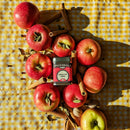 Nestled among fresh red apples on a yellow gingham cloth, Spicewalla Apple Pie Spice by Spicewalla is joined by cinnamon sticks, nutmeg, and cardamom pods scattered in bright sunlight—the ideal seasonal blend to elevate your fall baking.