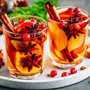 Two glasses filled with apple slices, cranberries, star anise, and The Spice Lab Organic Cinnamon Sticks on a tray, with some cranberries scattered nearby—perfect for serving a festive mulled wine or chai-inspired drink.