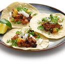 Three tacos on a plate topped with grilled meat, chopped onions, cilantro, and small pineapple pieces, perfectly seasoned with The Spice Lab Guajillo Chile Powder by The Spice Lab for authentic Mexican cooking, with lime wedges on the side.