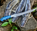 A Texan Knives Custom Handmade 13-Inch Damascus Steel Fillet Knife Blank with a resin handle rests on a tree stump beside three freshly caught fish, fishing line, and green leaves. Premium leather sheath included.