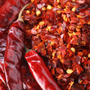 Whole dried red chili peppers displayed alongside a pile of The Spice Lab Organic Crushed Red Pepper Flakes, showcasing vibrant red hues and golden seeds—ideal for authentic Italian dishes and as a zesty pizza seasoning.