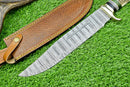 The Texan Knives Deluxe Dundee Knife—16" handmade Damascus steel blade, brass guard, and pakkawood or stag horn handle—rests beside its leather sheath on bright green grass.