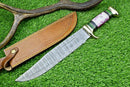 The Texan Knives Damascus Steel "The Bowie Knife" features a 16" blade, brass guard, resin pakkawood handle, and comes with a leather sheath, displayed on green grass next to an antler rack.