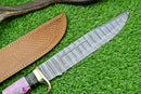 The Texan Knives Damascus Steel "The Bowie" Knife—16" with brass guard and resin pakkawood handle—rests beside its brown leather sheath on green grass.