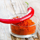 A fresh red chili pepper rests on a small glass bowl filled with vibrant The Spice Lab Ground Cayenne Pepper, set on a rustic wooden surface and highlighting the rich color and intensity of this quality bulk spice from The Spice Lab.