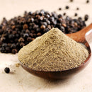 A wooden spoon holds a mound of The Spice Lab Butcher’s Cut Black Pepper, with whole black peppercorns from The Spice Lab scattered in the background on a light surface—perfect for adding robust seasoning.