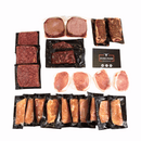 A selection of vacuum-sealed raw meats—including Kansas City Strip Steaks, boneless chicken breasts, American ground beef, and pork chops—from the Dude Food Gentleman’s Meat Box by Dude Food, arranged neatly on a white background next to a Dude Food card.