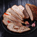 Sliced roasted pork with seasoning on a round dark slate plate, garnished with garlic cloves and a sprinkle of The Spice Lab Organic Crushed Red Pepper Flakes, set on a dark wooden surface—perfect for fans of Italian cooking.