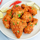 A plate of marinated chicken pieces seasoned with The Spice Lab Birdseye Chili Pepper Powder and garnished with cilantro, served with lime wedges and two red chili peppers on the side.