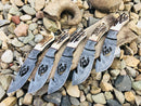 Five Texan Knives Deer Knives, each with a 10" wire-cut Damascus steel blade and antler horn handle, are displayed fan-like on rocks and driftwood outdoors. Each includes a leather sheath.