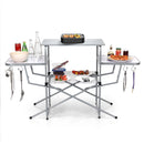 The DirectDeals Foldable Outdoor BBQ Table Grilling Stand features three main surfaces, metal legs, side hooks for utensils, a wire shelf below, and space for food and drinks—perfect for portable outdoor cooking.