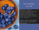 A wooden bowl and spoon filled with fresh blueberries sit beside text introducing Spice Wheel Blueberry Sugar by Spice Wheel, highlighting its fruity flavor and origins from high-quality dried blueberries or finely milled blueberry powder. The background alternates between blue and black sections with white lettering, emphasizing the perfect blend of granulated sugar and natural berry goodness.