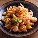 A plate of penne pasta with shrimp, sun-dried tomatoes, and herbs—including a touch of The Spice Lab Organic Oregano Leaf by The Spice Lab—garnished with a sprig of fresh basil and served on a dark ceramic dish, highlighting the vibrant flavors found in Mediterranean cooking.