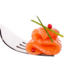 A silver fork holds rolled slices of smoked salmon, garnished with two chive stalks and The Spice Lab Pink Pepper Berries (Whole) Brazilian Pink Peppercorns, on a white background.