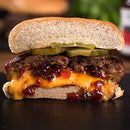 A juicy cheeseburger cut in half, with melted cheddar, pickles, and a layer of Terrapin Ridge Farms Hot Pepper Bacon Jam - 5 oz inside the patty, all nestled in a soft hamburger bun.