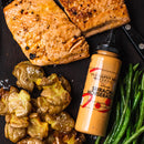 Grilled salmon, crispy smashed potatoes, and green beans are served with a bottle of Terrapin Ridge Farms Sriracha Horseradish Garnishing Squeeze Sauce—the perfect creamy dip for extra kick—all arranged on a dark surface.
