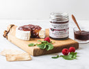 A round of brie topped with Terrapin Ridge Farms Hot Pepper Raspberry Preserves sits on a wooden board with crackers, fresh raspberries, greens, and a jar labeled "Terrapin Ridge Farms.