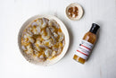 A bowl of raw, marinated shrimp sits on a white surface next to a small dish of red pepper flakes and a bottle of Terrapin Ridge Farms Tropical Tequila sauce.