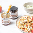 Open and closed jars of Terrapin Ridge Farms Apple Maple Bacon Jam with a knife, apple slices topped with cheese and walnuts, and cheese crumbles—perfect for charcuterie boards or pairing with this savory bacon jam.