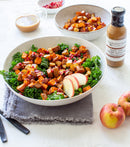 A bowl of kale salad with roasted sweet potatoes, apple slices, pomegranate seeds, and Terrapin Ridge Farms Apple Cider Maple Balsamic Vinaigrette. Nearby: fresh apples, extra sweet potatoes, and the flavorful Terrapin Ridge dressing.
