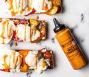 Three pieces of toast with sliced tomatoes, poached eggs, microgreens, and creamy sauce are arranged beside a bottle of Terrapin Ridge Farms Spicy Chipotle Garnishing Squeeze on a white surface.