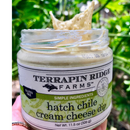A hand holds an open jar of Terrapin Ridge Farms Hatch Chile Cream Cheese Dip outdoors, showcasing its creamy texture. The label spotlights gluten free and simple ingredients for this delicious Southwest-inspired dip by Terrapin Ridge Farms.