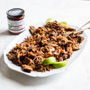 A white platter with shredded, sauced meat and lime wedges sits beside a jar of Terrapin Ridge Farms Jalapeno Hatch Chile Jam, adding sweet heat from Terrapin Ridge Farms to the dish on a light background.