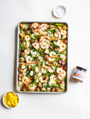 A sheet pan holds roasted shrimp, red potatoes, and green beans. Nearby are salt, diced yellow peppers, a jar of spice blend, and Terrapin Ridge Farms Mango Habanero Jam to add sweet heat to your appetizers.