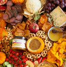 A vibrant autumn charcuterie board with cheeses, crackers, salami, grapes, pretzels, nuts, and fresh and dried fruit, highlighted by Terrapin Ridge Farms Raspberry Honey Mustard Quart, surrounded by fall leaves and small pumpkins.