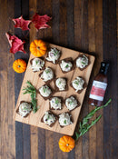 A wooden board with appetizers topped with chicken salad sits on a table, perfect for holiday entertaining. Small pumpkins, red maple leaves, rosemary sprigs, and a bottle of Terrapin Ridge Farms Tart Cherry, Apple and Rosemary Glaze complete the display.