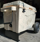 A tan and gray Taiga Coolers Ice Chest with the Taiga Coolers Ice Chest Wheel Kit for 55quart and 88 quart coolers and black handles rests on a black metal stand in a sunlit garage.