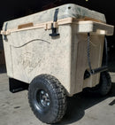 A Taiga Coolers Ice Chest Wheel Kit for 55quart and 88 quart coolers, featuring rugged wheels, sits on a sunny concrete floor beside a beige and gray speckled Taiga Coolers ice chest with black latches and rope handle.