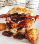 A biscuit sandwich with crispy fried chicken, bacon, and Terrapin Ridge Farms' Blueberry Bourbon Pecan Jam, served with extra jam and tater tots—a creative breakfast spread featuring Terrapin Ridge Blueberry Bourbon Pecan Jam in the background.