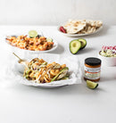 Three shrimp tacos with avocado and sauce sit on parchment in the foreground. In the background, shrimp, flatbread, fresh slaw, sliced avocado, a lime wedge, and Terrapin Ridge Farms Nashville Hot Mustard complete the scene.