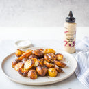 Crispy roasted potatoes are served on a white surface, with a bottle of Terrapin Ridge Farms Truffle Aioli Squeeze behind the plate, a small bowl of salt nearby, and a striped towel to the right.