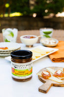 Terrapin Ridge Farms Mango Habanero Jam is served with crackers, cheese, drinks, and an orange napkin—ideal for sweet heat appetizers. Slices of bread topped with this gourmet jam and almonds sit on a wooden board in front.